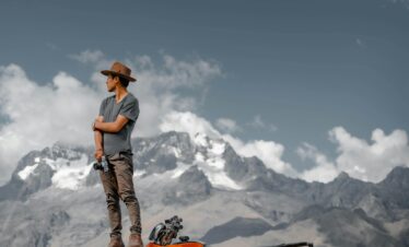 A man in a hat stands on a quad, set against Peru's dramatic Cusco mountains. Adventure and exploration.
